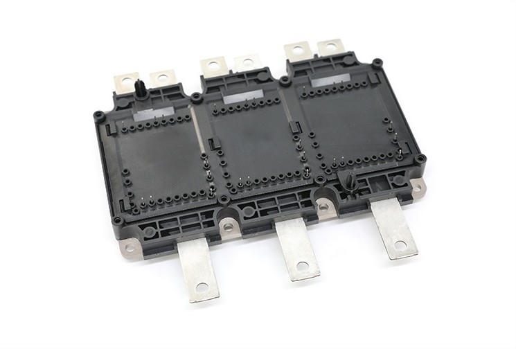 A black insert-molded plastic housing with rows of metal pins and six flat metal terminals, photographed on a white background