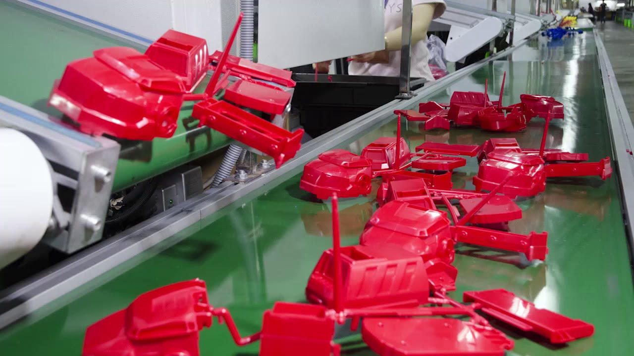 Freshly molded red plastic parts, still joined by their runners, moving along a green conveyor away from the molding press