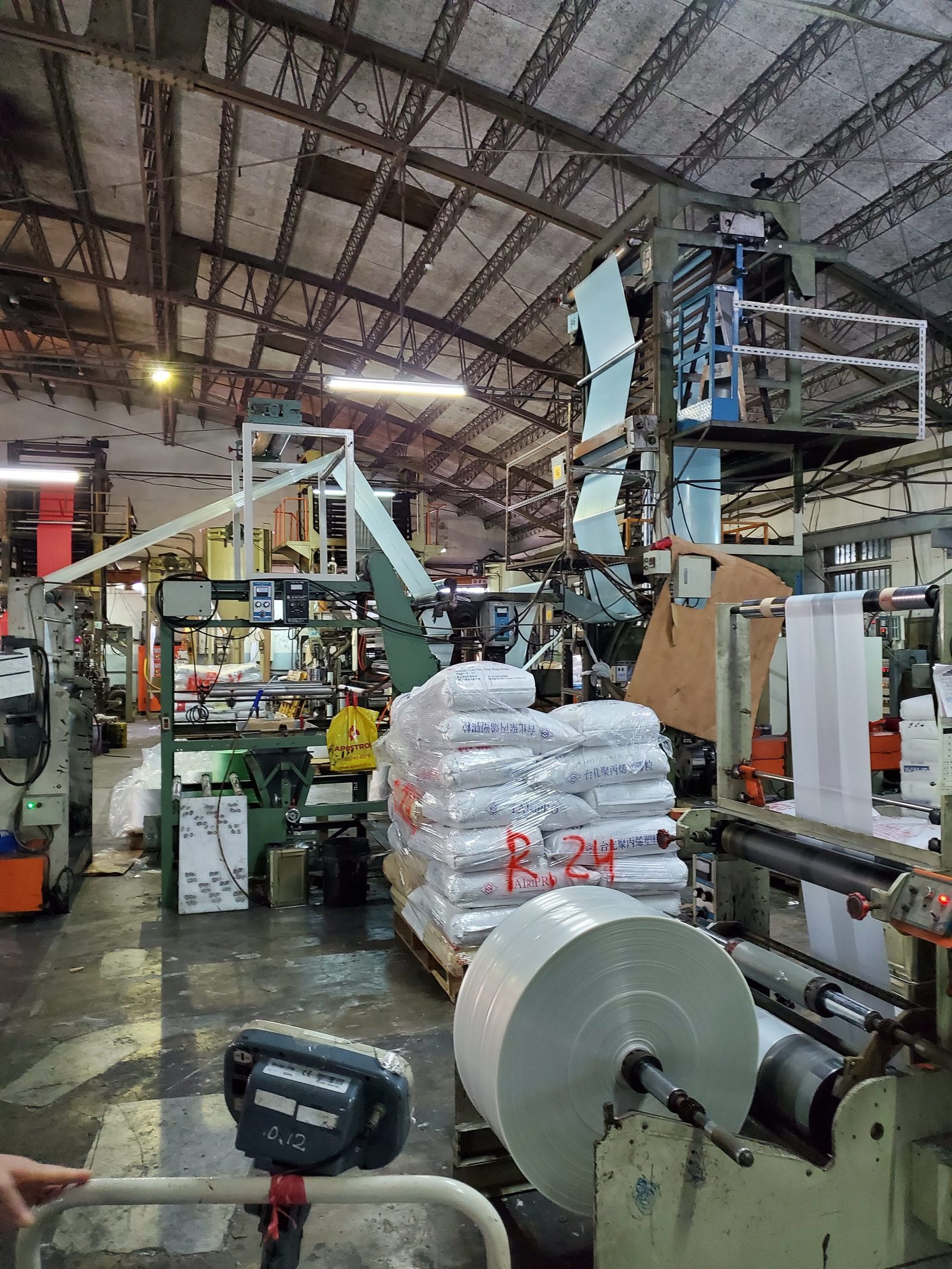 Sacks of plastic resin pellets stacked on a pallet and marked by lot in red marker on a partner factory floor, with film rolls in front