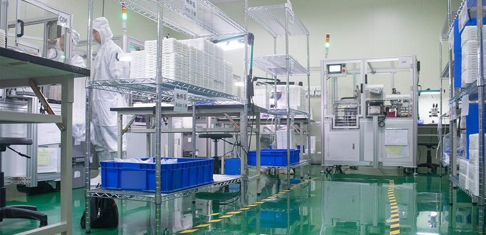 A cleanroom molding area with a gowned operator, wire racks of white molded trays, blue parts bins and an automated cell on a green epoxy floor