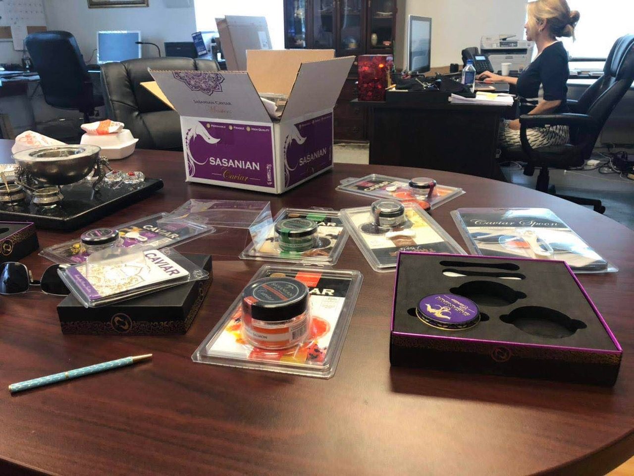 Printed tins, a blister card, a black presentation box with a fitted insert and a purple shipping carton laid out on a conference table for review