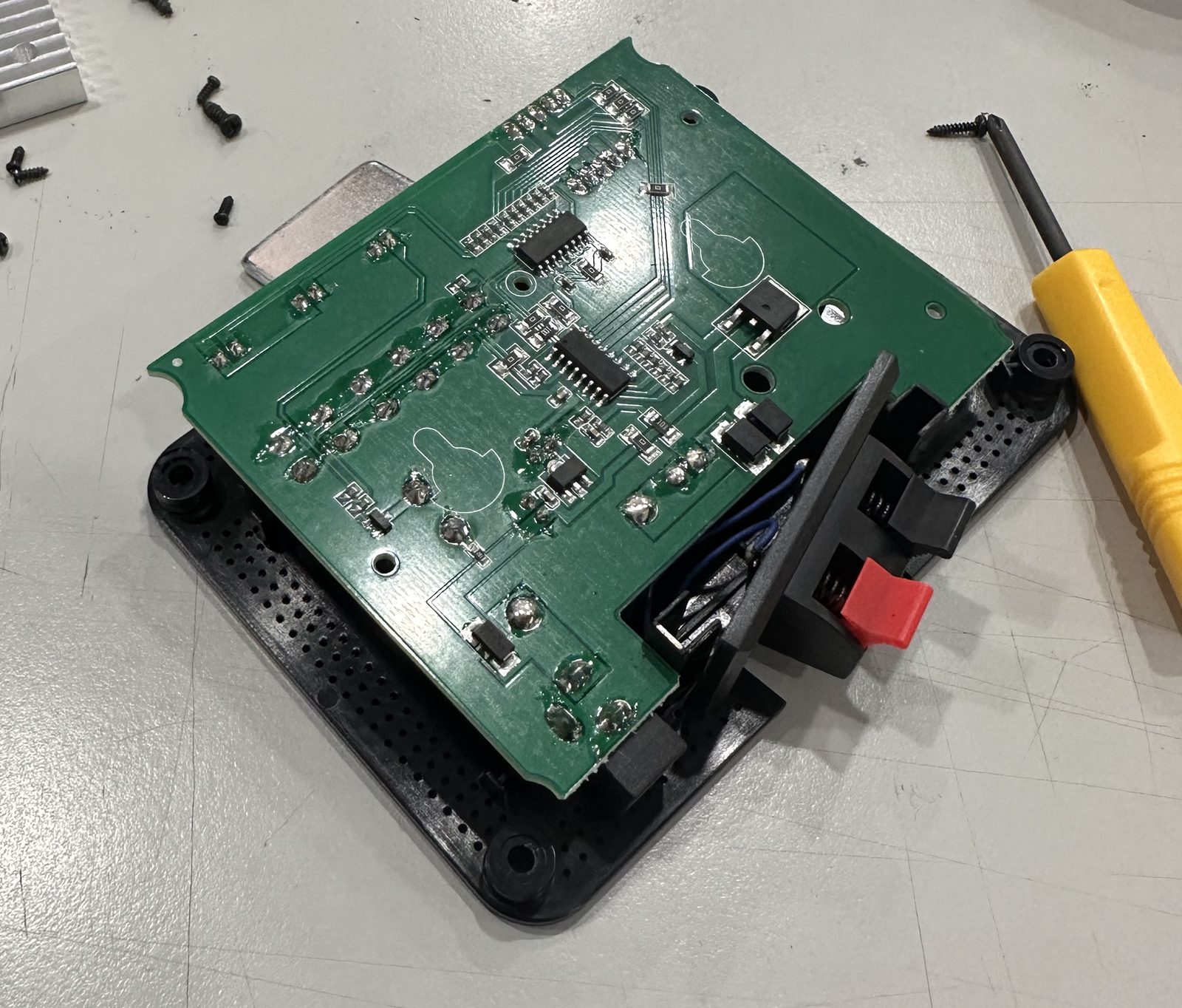 A green circuit board lifted off a black molded plastic base with screw bosses at the corners, small screws on the bench