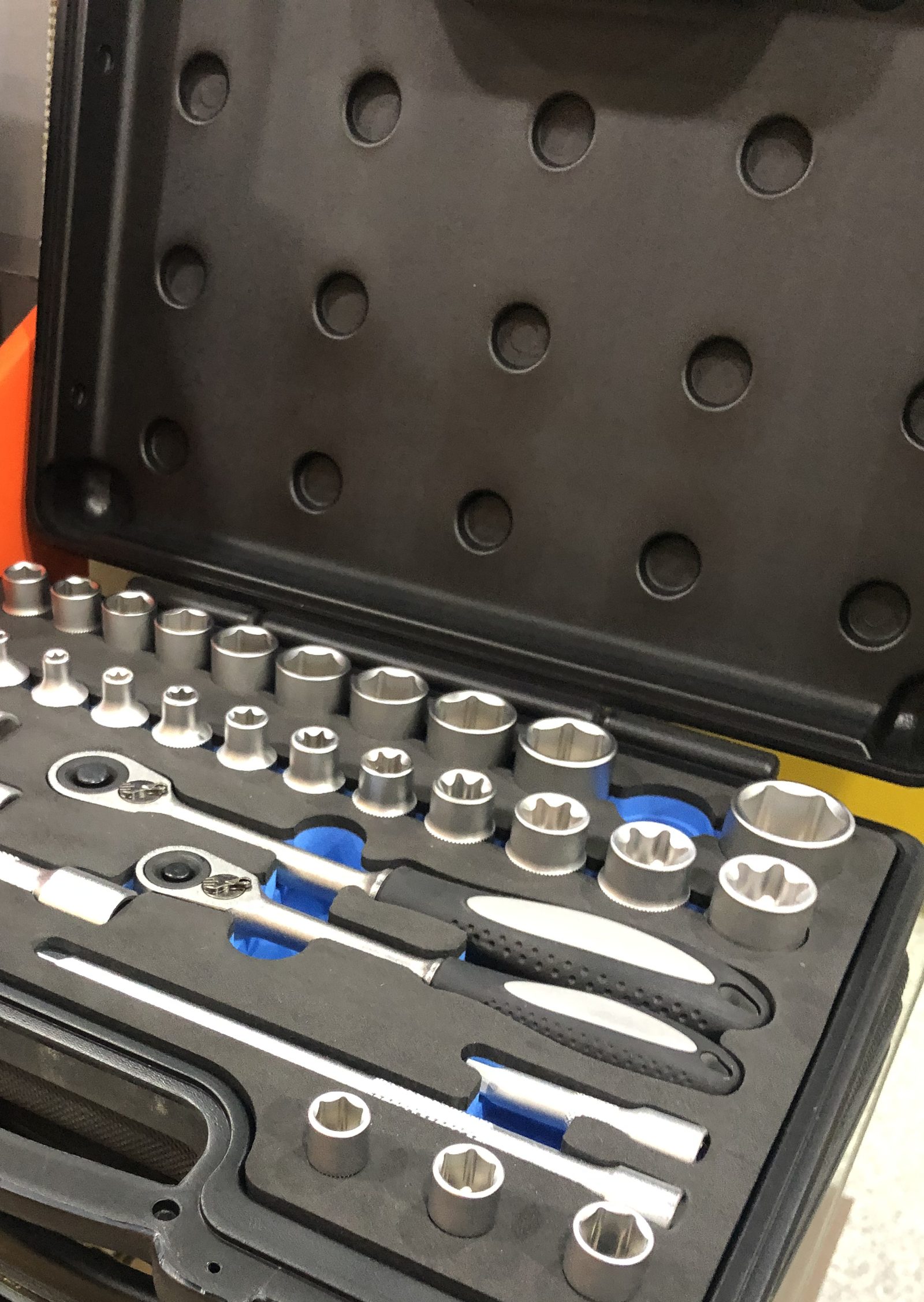 The open lid of a black molded carry case with rows of round molded pockets, above a socket set in a foam tray