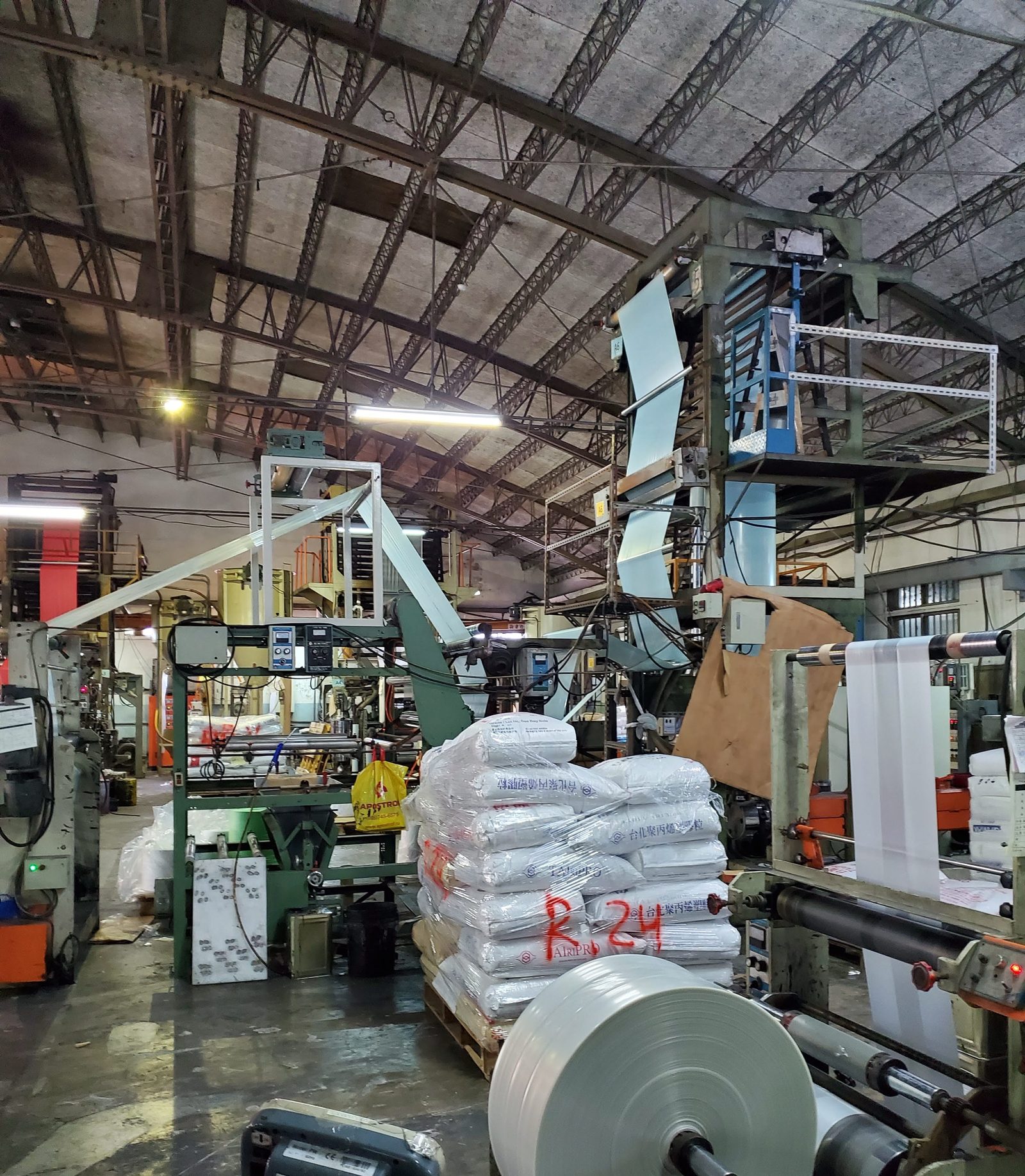 A plastic film extrusion line with a roll of film on the winder and pallets of resin bags in the aisle