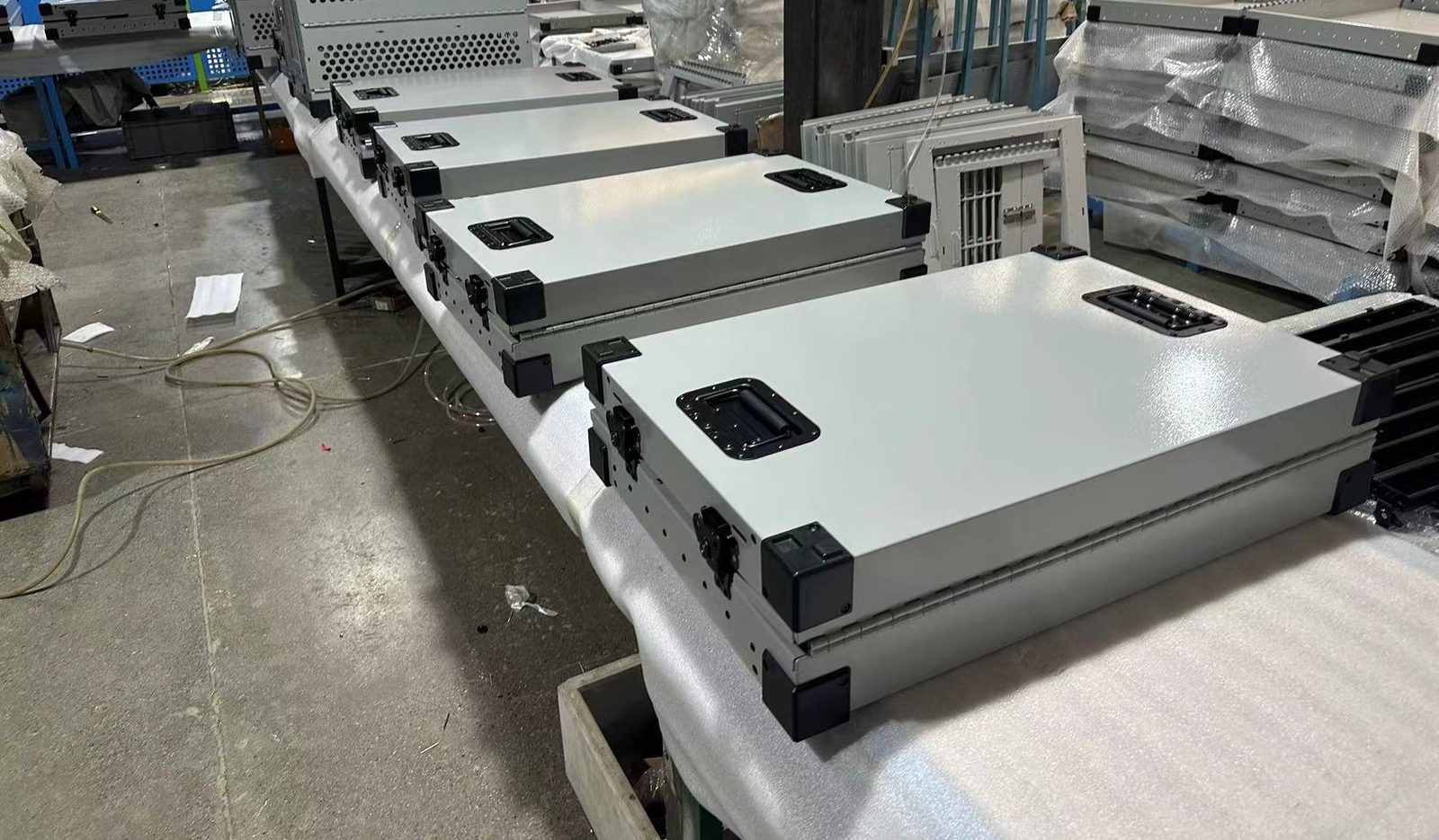 Powder-coated sheet metal enclosures with latches and corner guards lined up on a padded bench mid-assembly