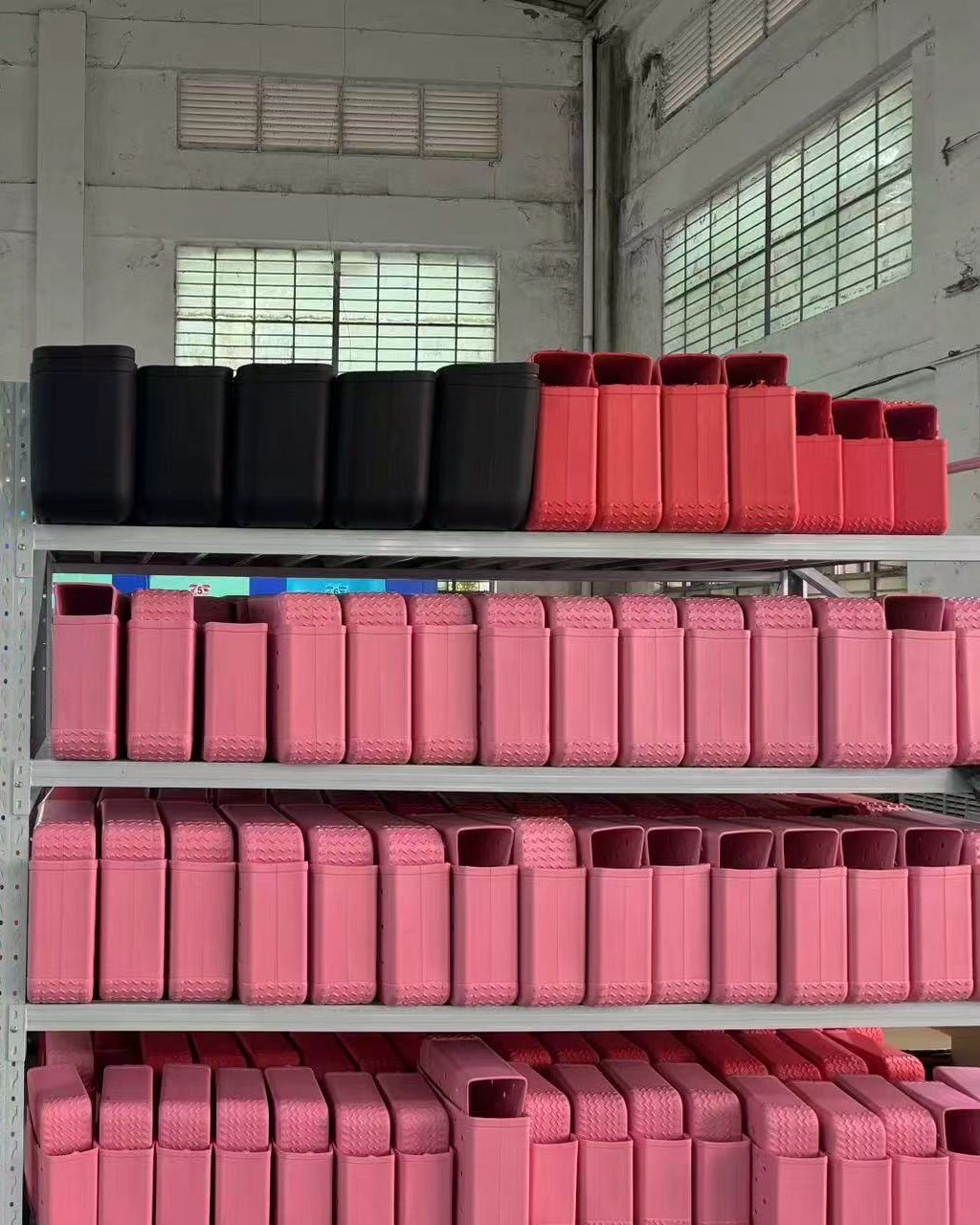 Shelves of red, pink and black molded plastic parts stacked by color in a factory building