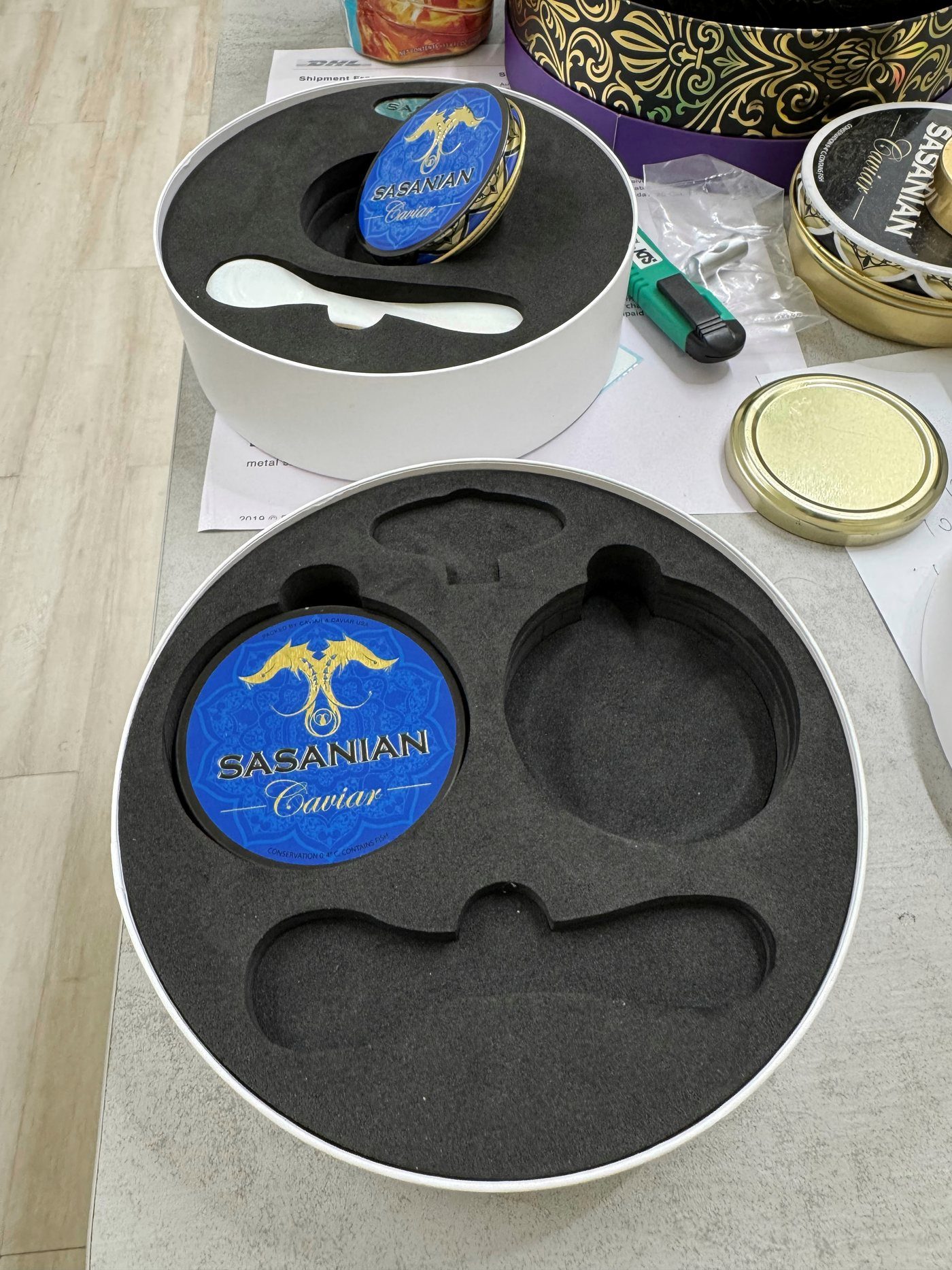 Round presentation boxes with die-cut black foam inserts shaped to hold a caviar tin and a spoon