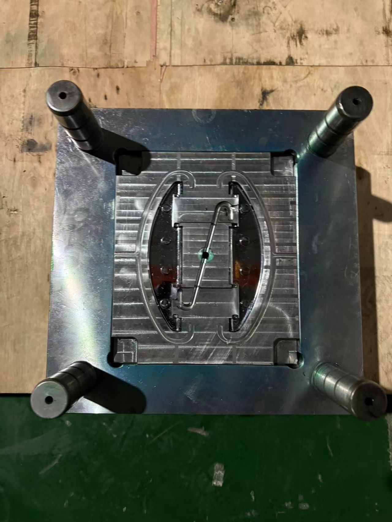 One half of a small single-cavity injection mold on a bench, the cavity insert set in the plate and four leader pins at the corners