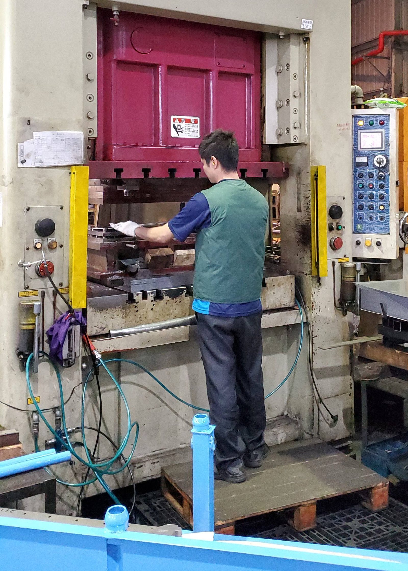 An operator in work gloves loading blanks into a die set in a large press