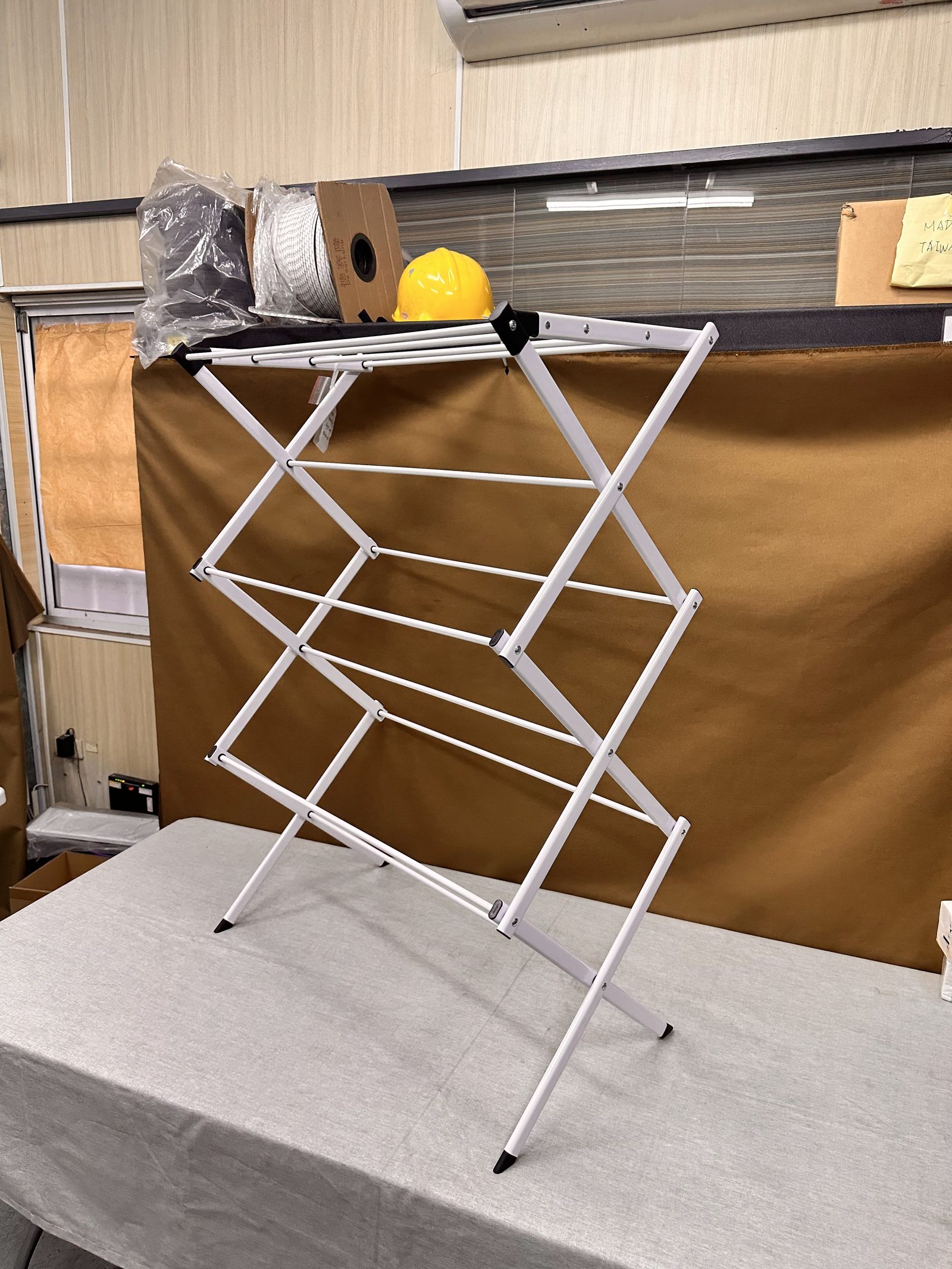 A white folding drying rack sample standing on a covered table in a sample room