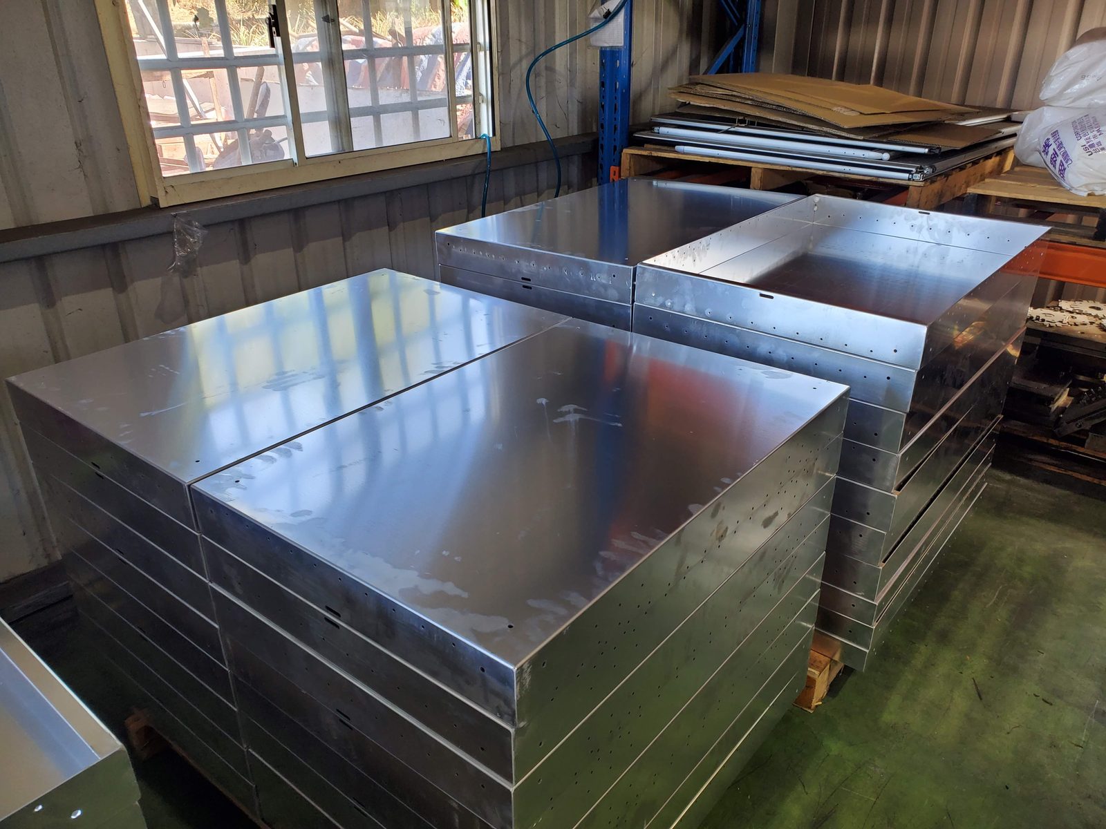 Brushed stainless steel cabinet shells stacked on pallets in a factory, a finished lot waiting to be checked and packed