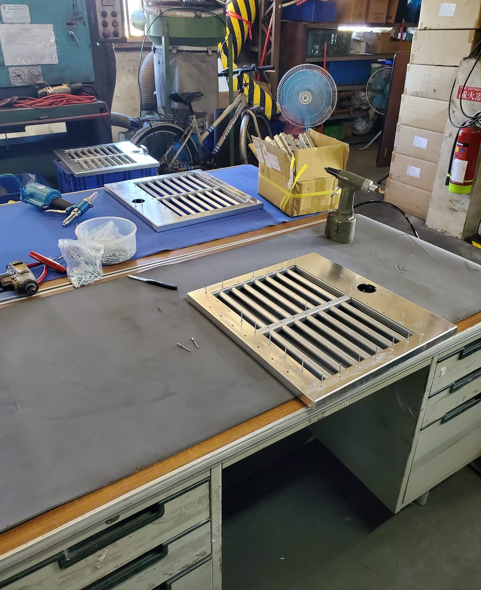 An assembly bench with half-riveted stainless grilles and hand tools, work in progress at a factory