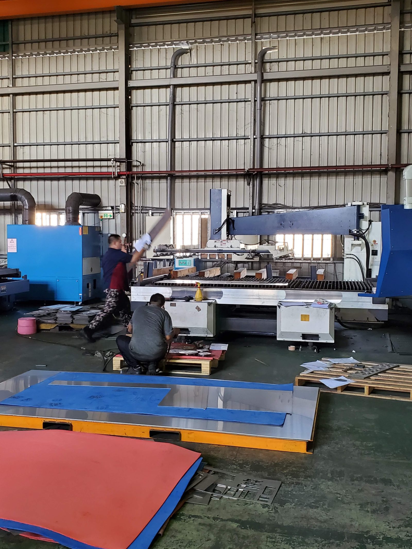 Workers loading sheet stock onto a CNC cutting table, the kind of scene to ask for on a factory video walk-through