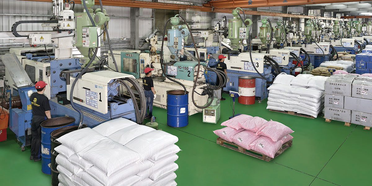 A row of numbered injection molding machines and resin sacks on a real factory floor