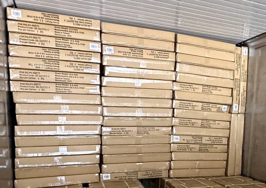 Export cartons stacked in a shipping container, side marks showing PO number, product code, gross weight, measurement, pieces per carton and the country of origin