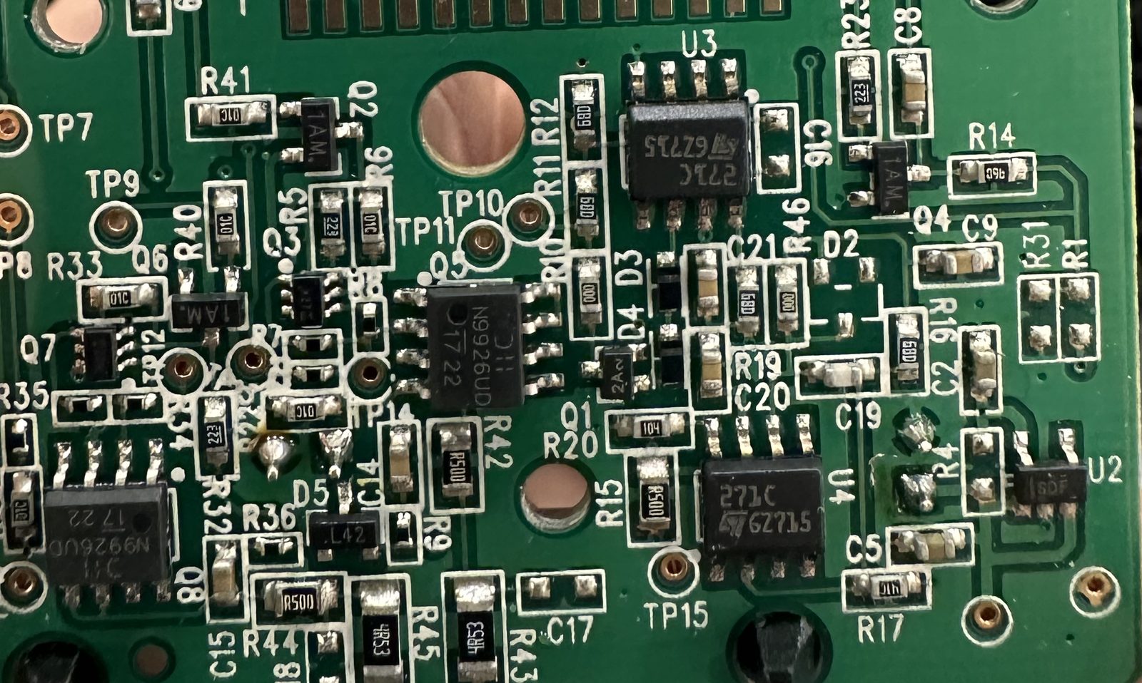 Close-up of an assembled green circuit board: surface-mount chip resistors and capacitors, small three-lead transistors, eight-lead SOIC chips and round gold test points