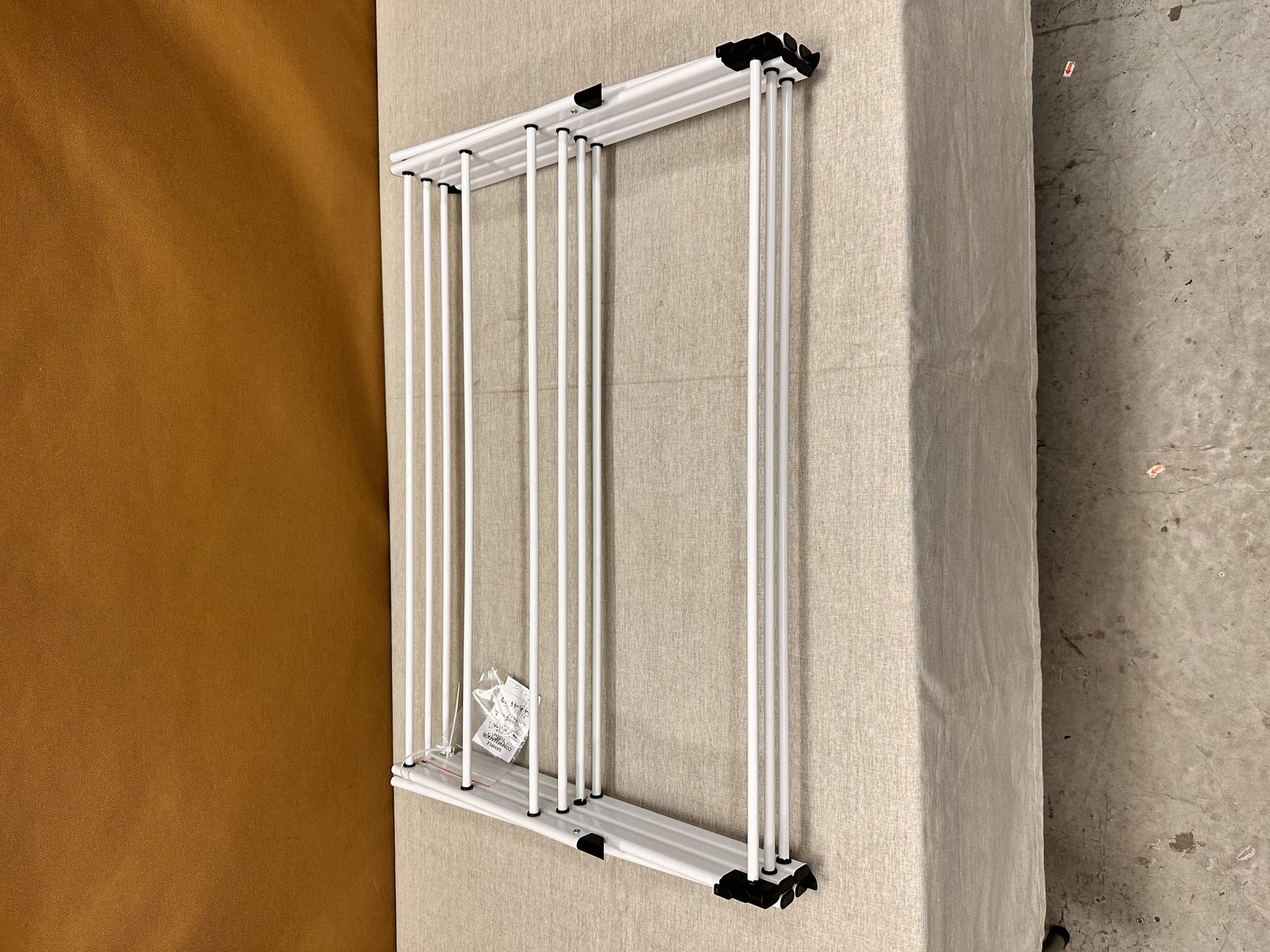 A white folding rack frame laid flat on a covered inspection table, hardware bag still attached