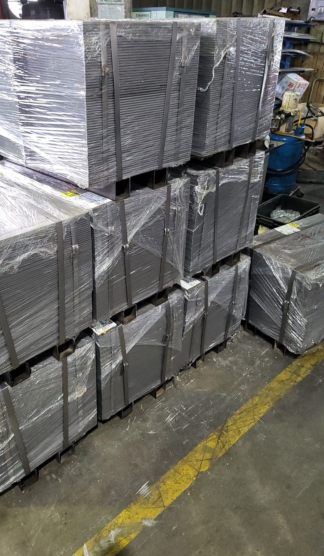 Bundles of steel sheet blanks strapped and shrink-wrapped on pallets in a factory