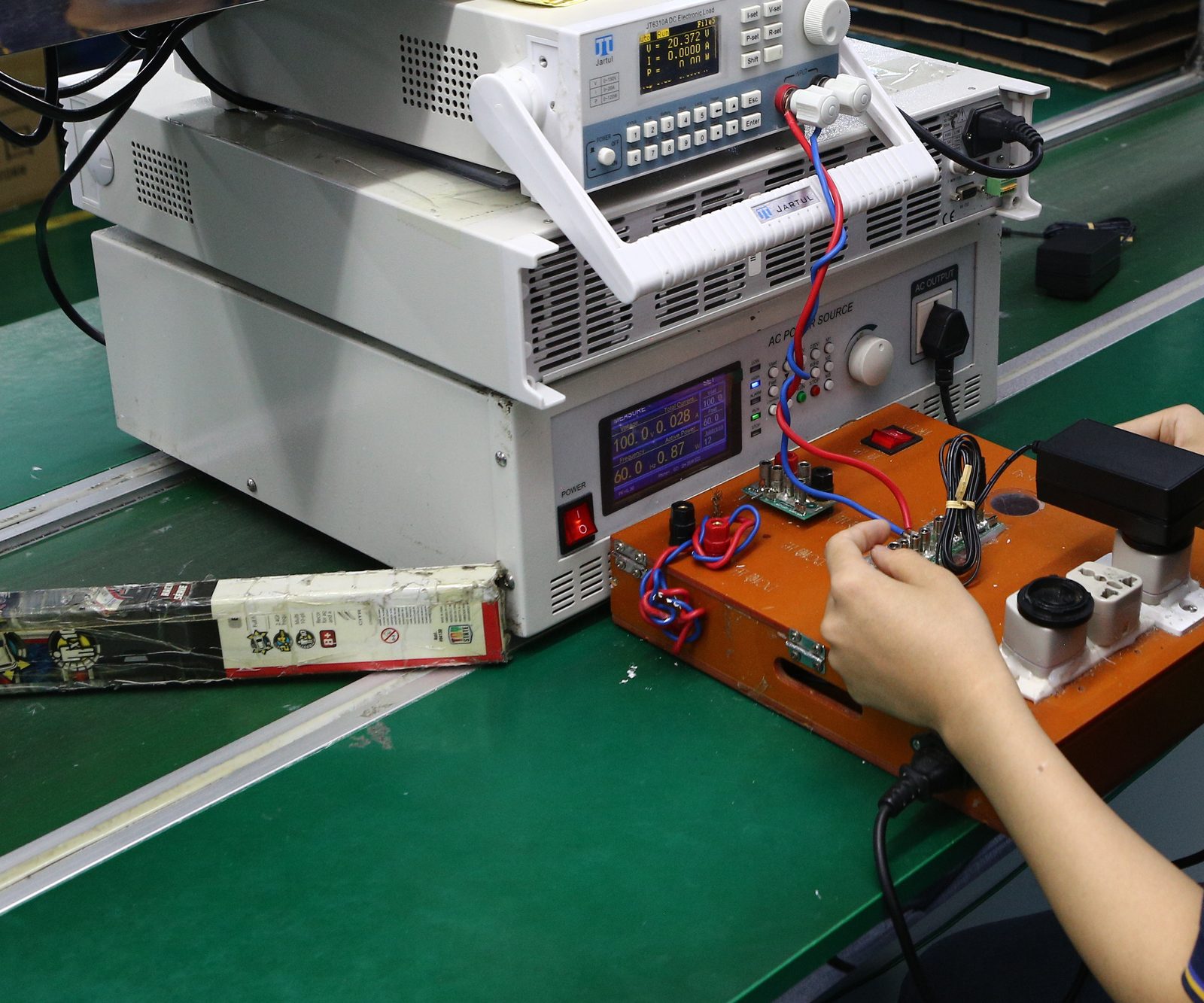 An electrical test fixture wired to bench instruments on an electronics assembly line