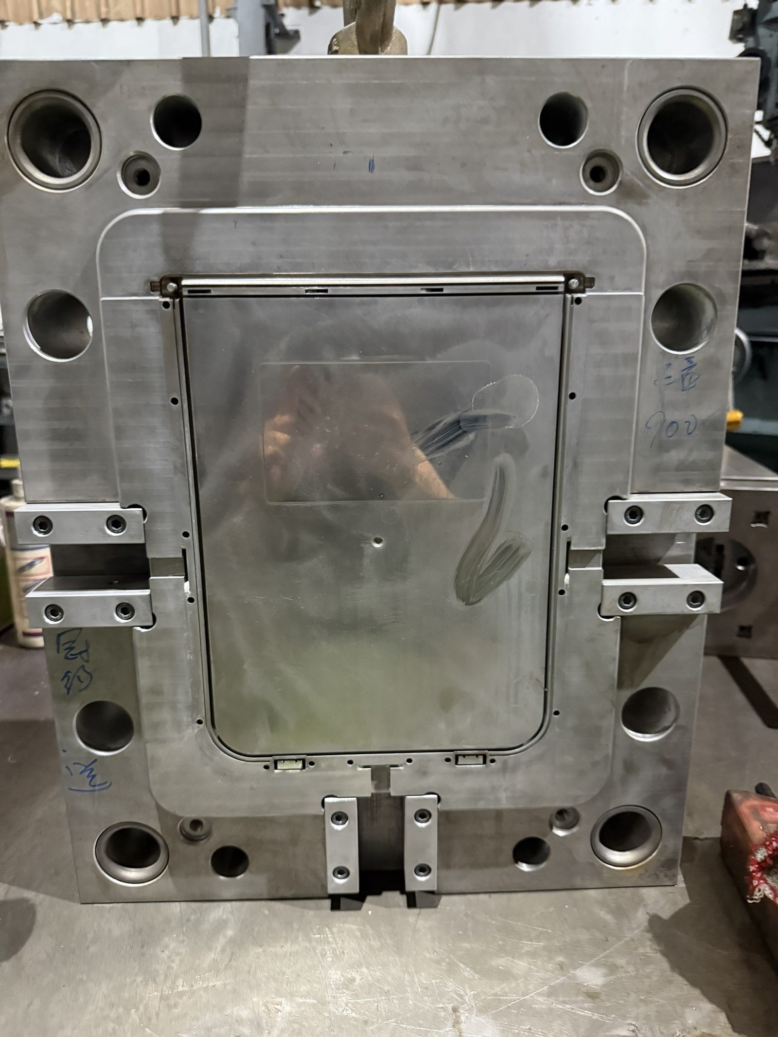 A large steel mold plate standing on the shop floor, with a polished rectangular cavity and marker notes on the steel