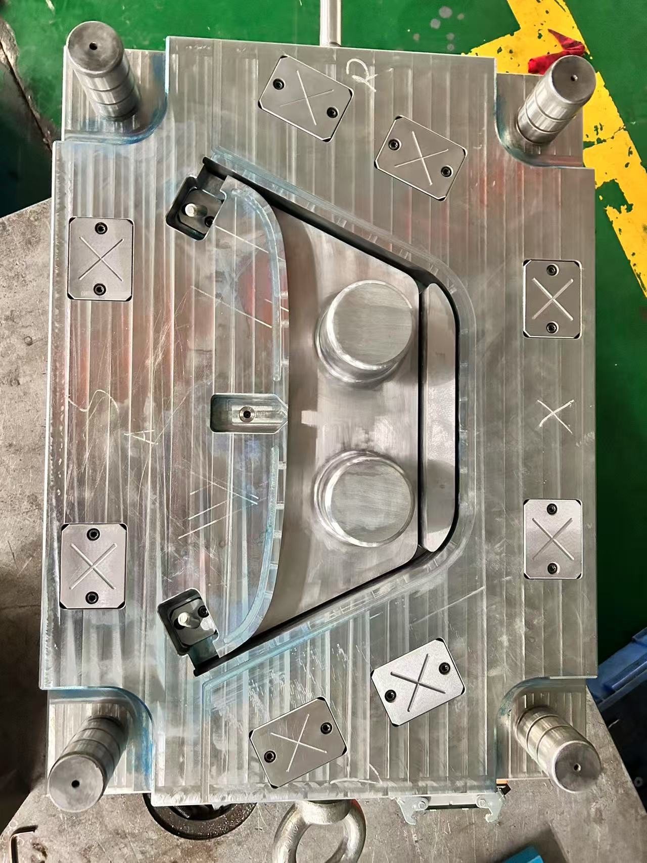 A steel mold half on a bench with a shaped cavity outline, two round cores and guide pillars at the corners