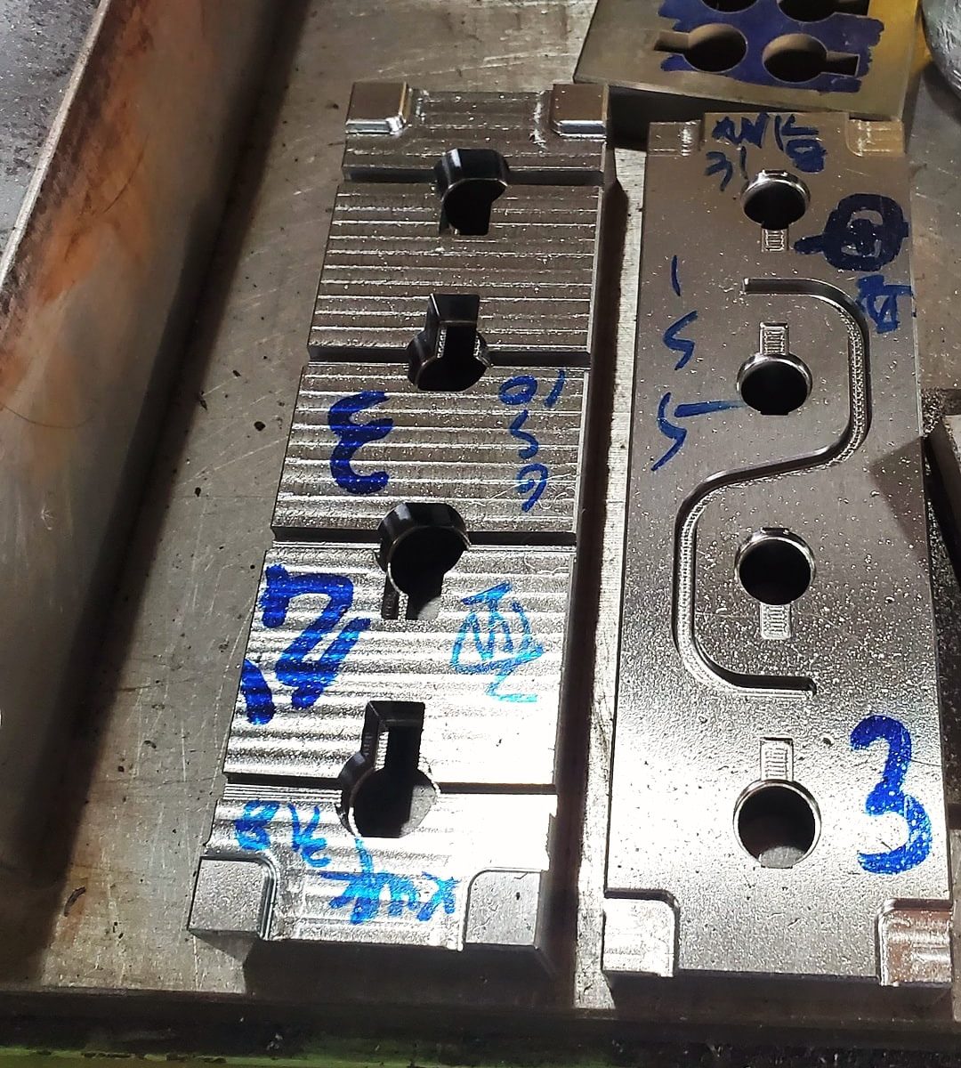 Steel mold inserts with machined cavities and marker notes on a toolroom bench