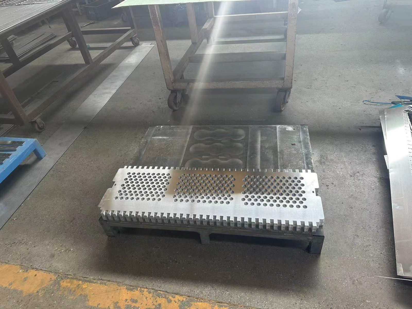 A steel tool plate with three machined cavities on a pallet, a punched perforated panel resting on top