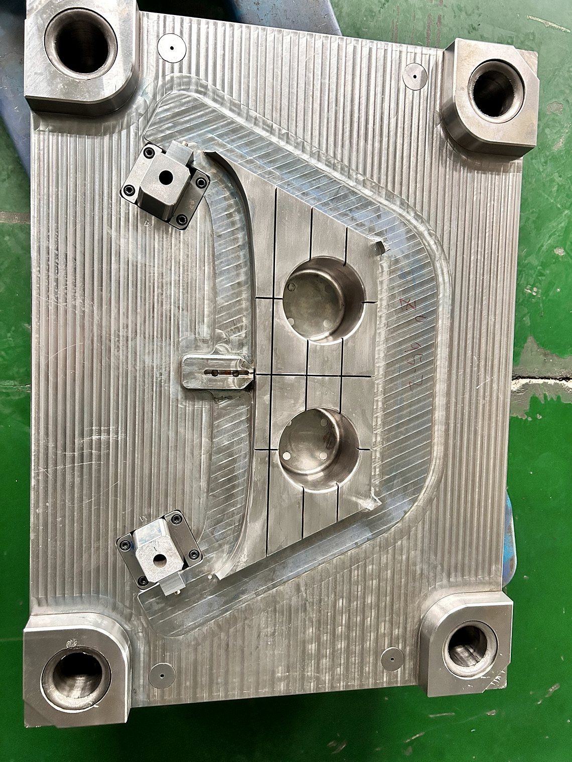 A machined mold plate with two round cavity pockets, guide bushings and locating blocks on the shop floor
