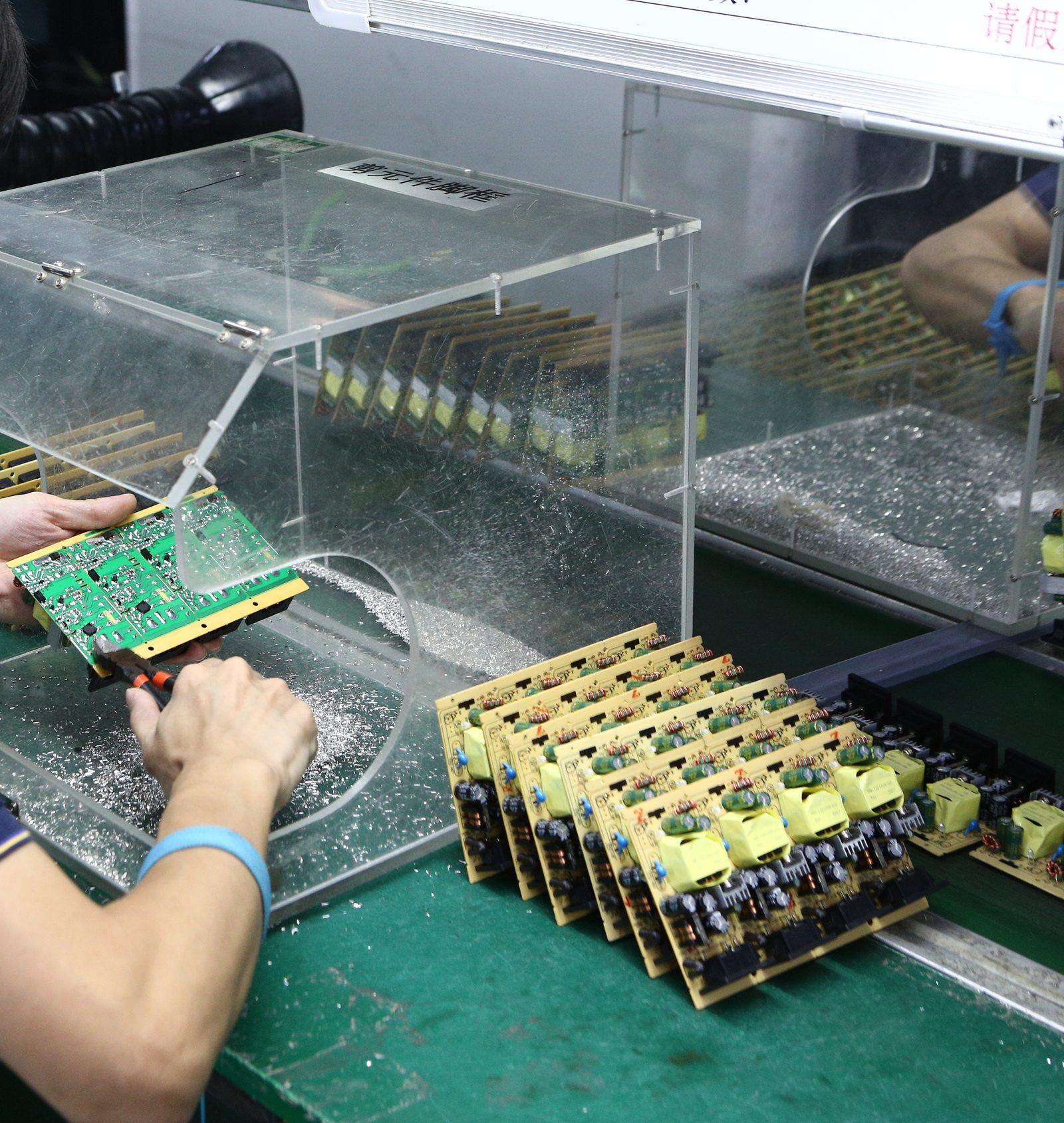 Hands holding a printed circuit board assembly for inspection, a row of finished boards on the bench