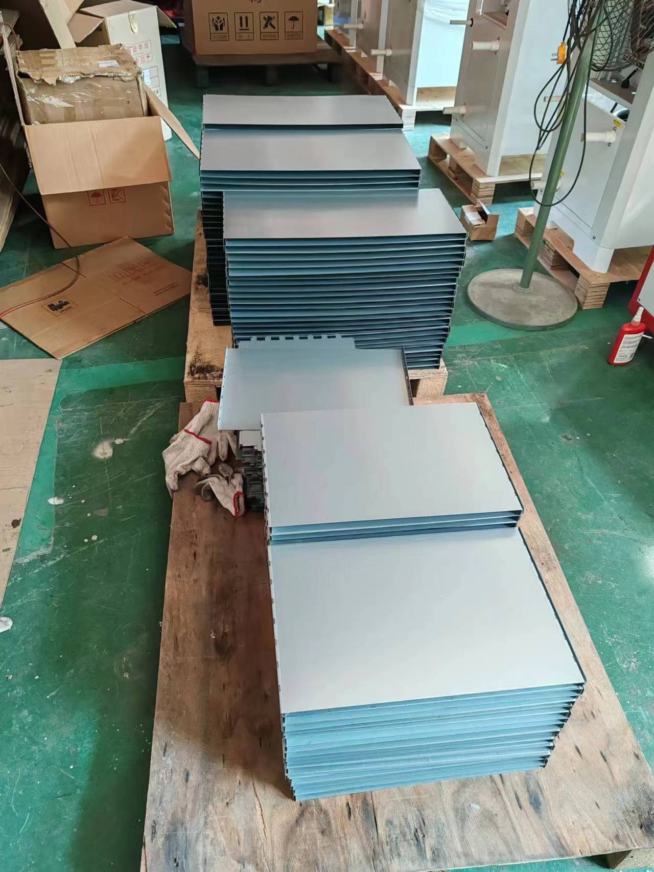 Stacks of blue-gray powder-coated steel panels on a wooden pallet on the shop floor