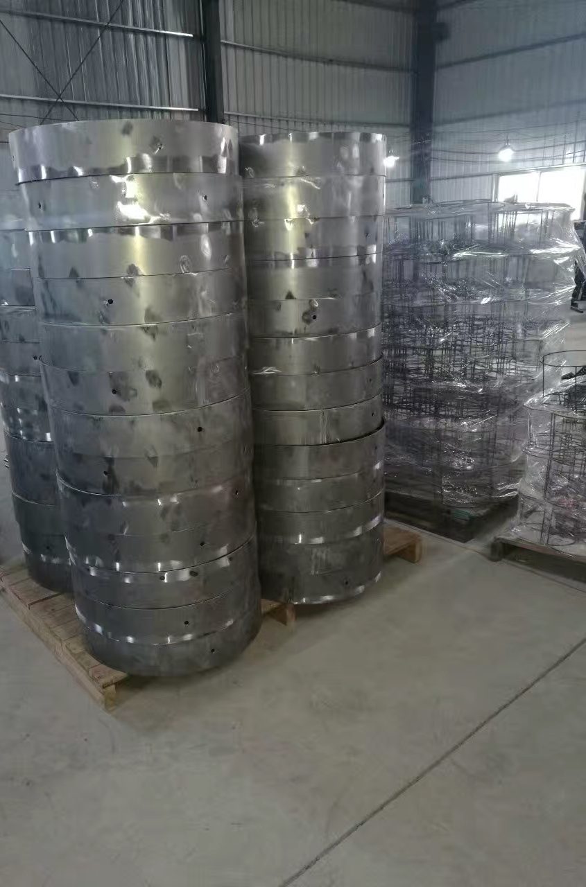 Rolled and punched stainless steel rings stacked high on wooden pallets in a fabrication warehouse