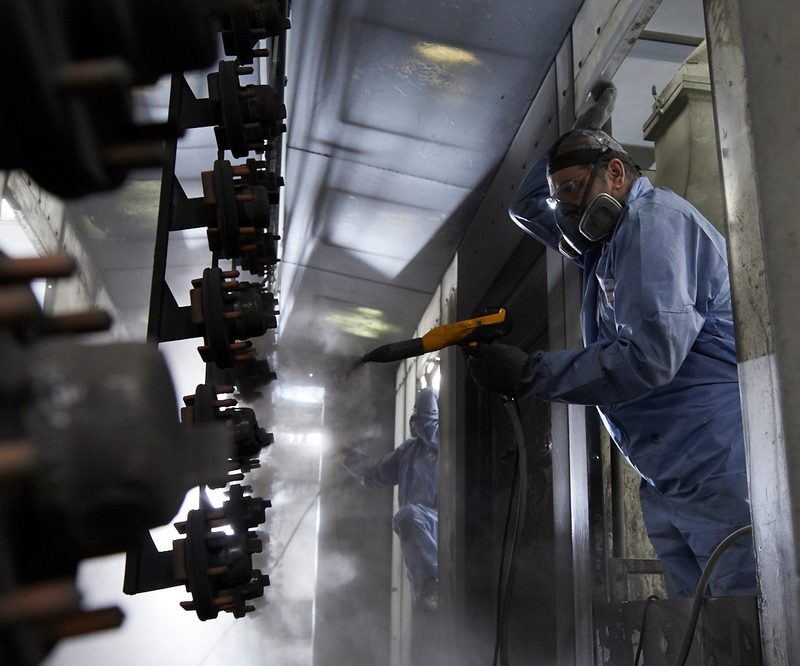 Hanging hubs move through a narrow spray tunnel while operators coat both sides.