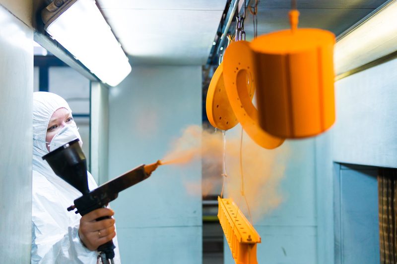 Discs, a cylinder and a bar hang from the line as orange powder is applied.