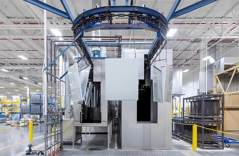 An automated overhead loop carries large panels into the spray and oven tunnel