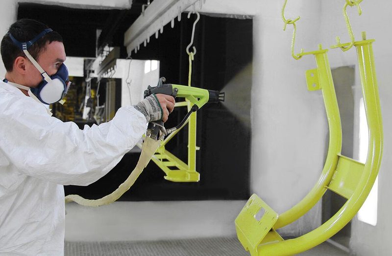 A bent-tube bracket is coated yellow while other hanging parts wait behind.