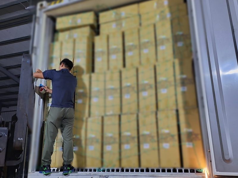 A worker netting a wall of master cartons inside a shipping container at a factory in Taiwan