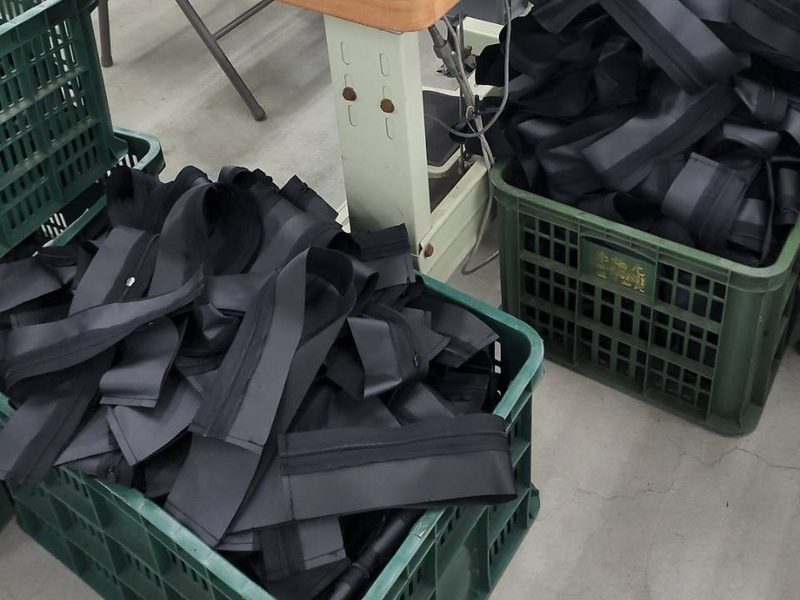 Crates of cut black webbing and strap parts beside a sewing station