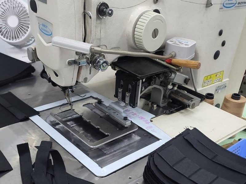 A programmable pattern sewing machine stitching black webbing held in a steel template