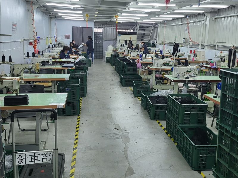 Rows of industrial sewing machines with green bins of cut parts on a sewing floor in Taiwan