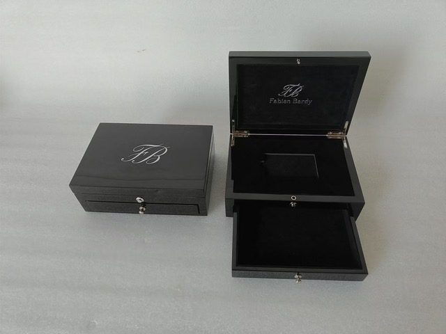 A black wooden presentation box with an engraved monogram and a lower drawer