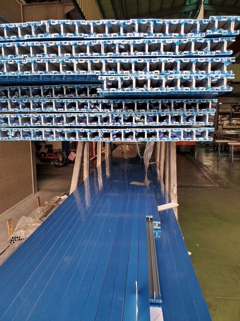 Aluminum extrusion lengths, film-wrapped, stacked on the floor.