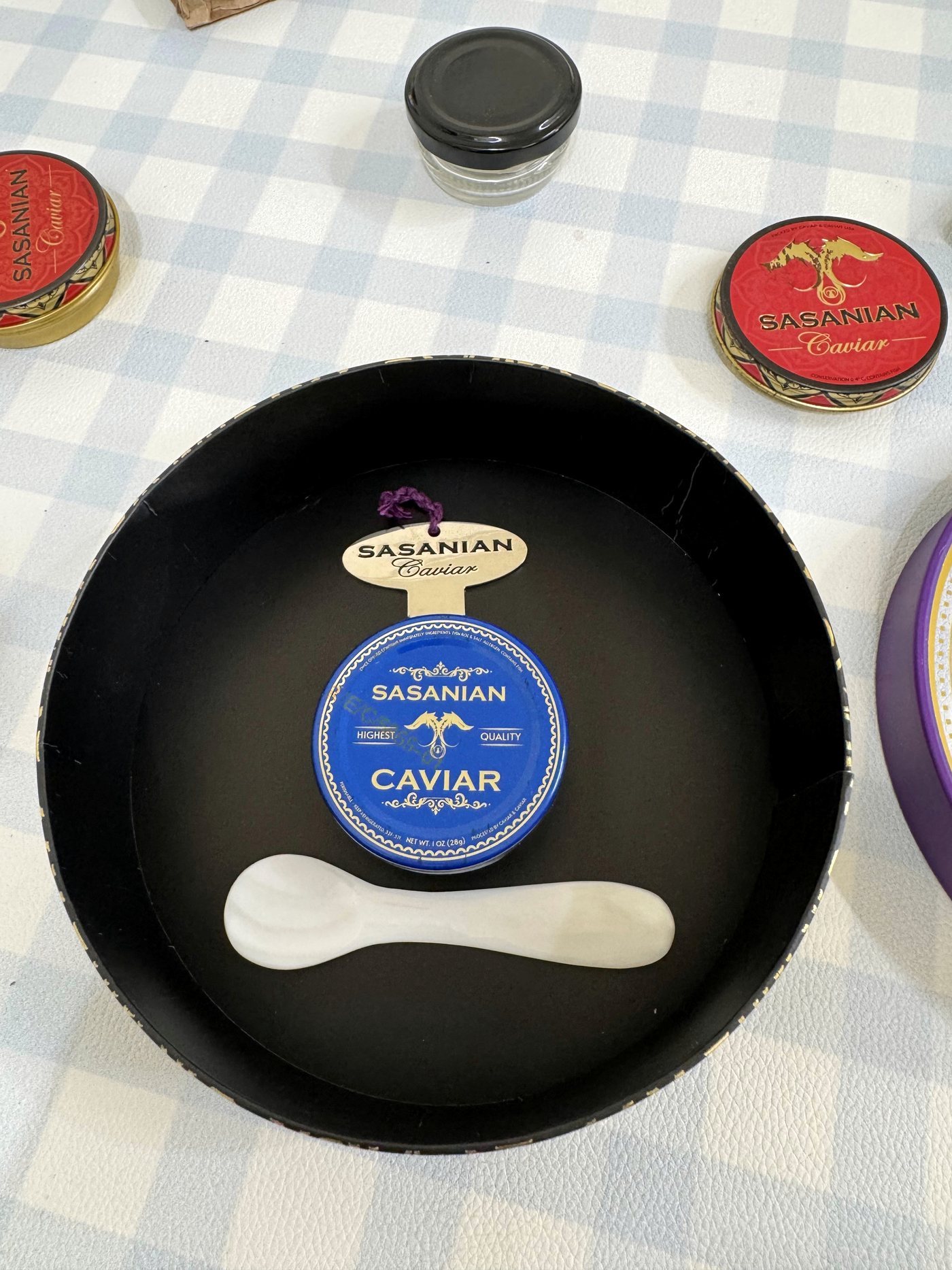 A black round presentation box holding a caviar tin and spoon