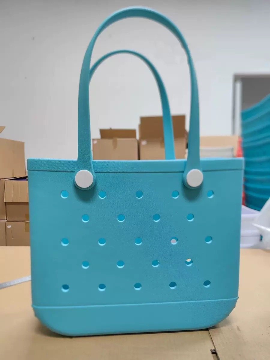 A molded plastic tote bag with white button handles on a factory bench