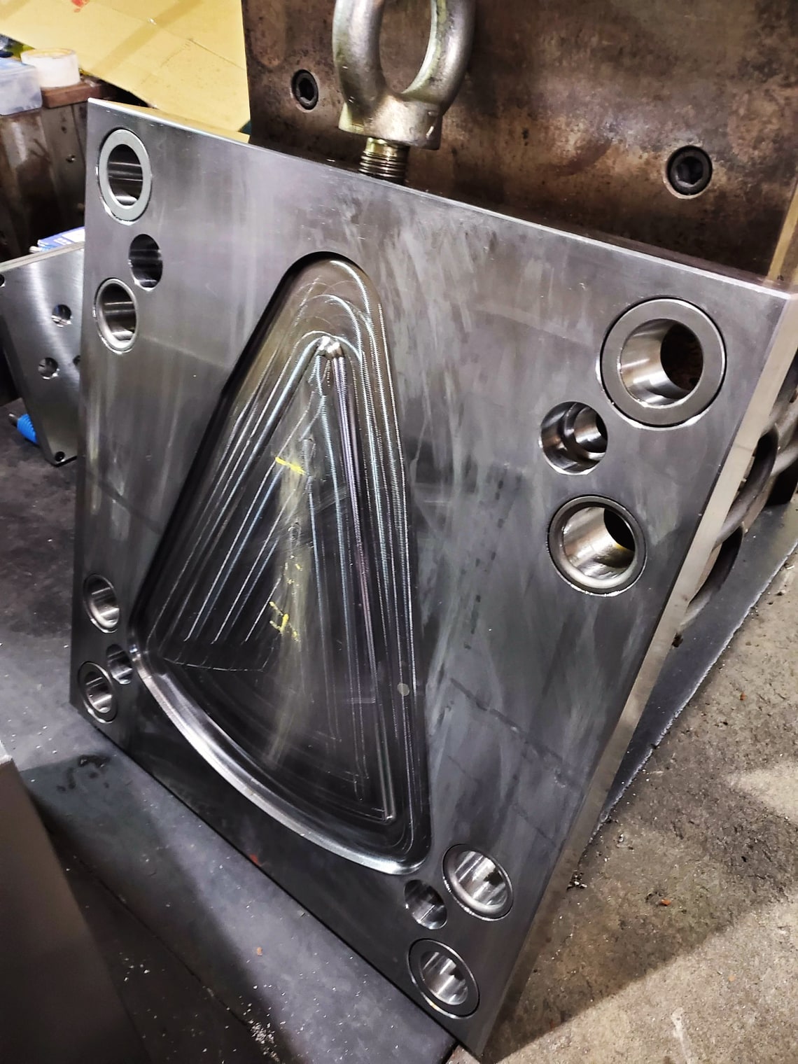 A steel mold plate with a triangular cavity, lifted on an eyebolt