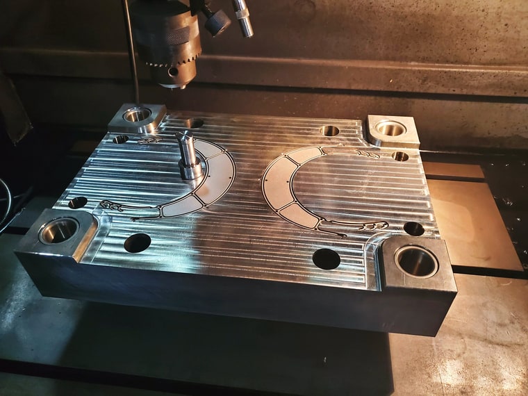 A machined steel mold plate on the bed of a milling machine